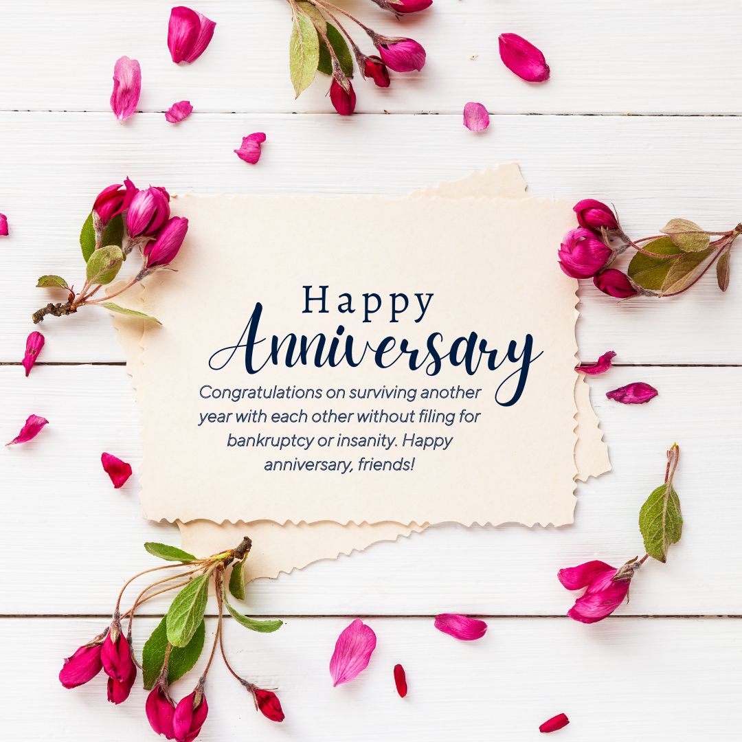 Anniversary card with humorous wedding anniversary wishes for friends, surrounded by pink petals on a white wooden background.