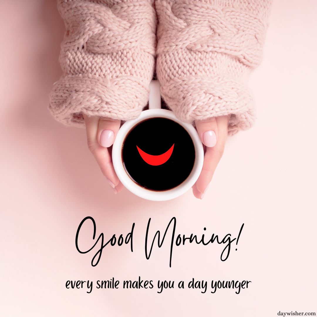 Top view of two hands holding a coffee mug with a smile design at the bottom, on a pink background with the text "Good morning images! Every smile makes you a day younger.