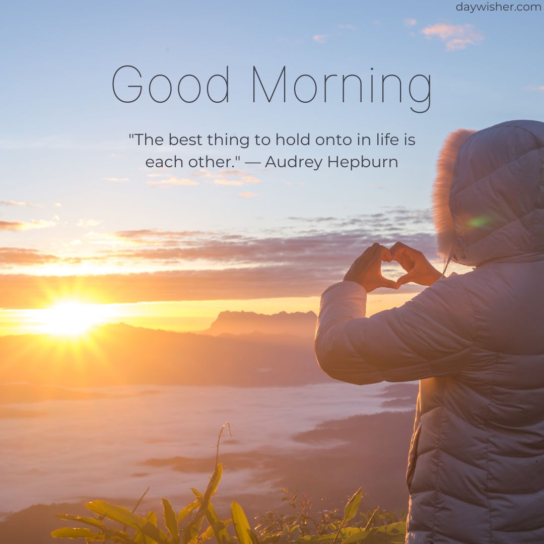 A person in a winter coat forms a heart shape with their hands against a sunrise in the mountains, accompanied by a "Good Morning" quote from Audrey Hepburn: "The best thing to hold onto