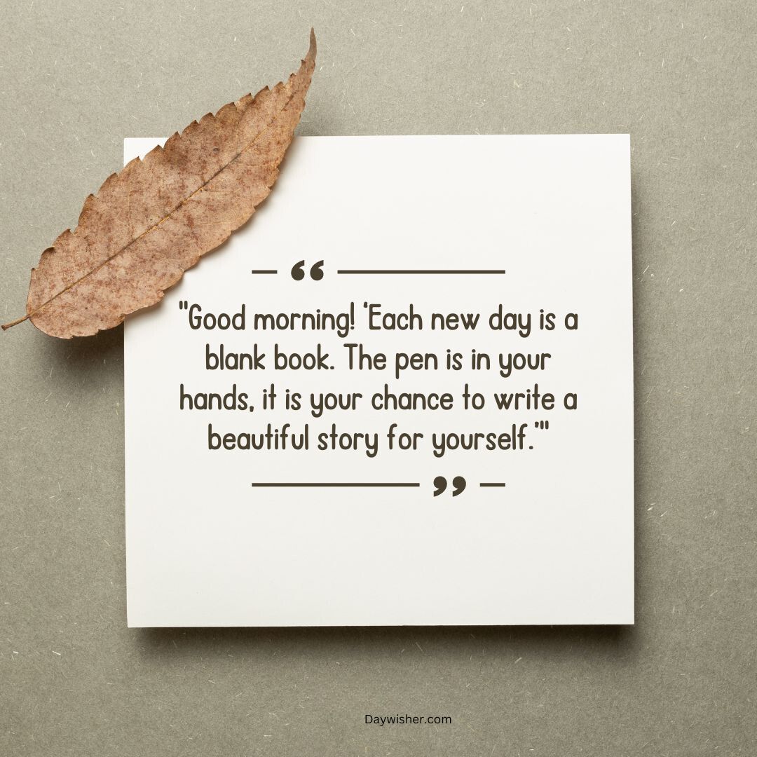 An inspirational quote on a white paper note with a dry leaf on top, against a textured beige background, saying, "good morning! each new day is a blank book. the chance to write a