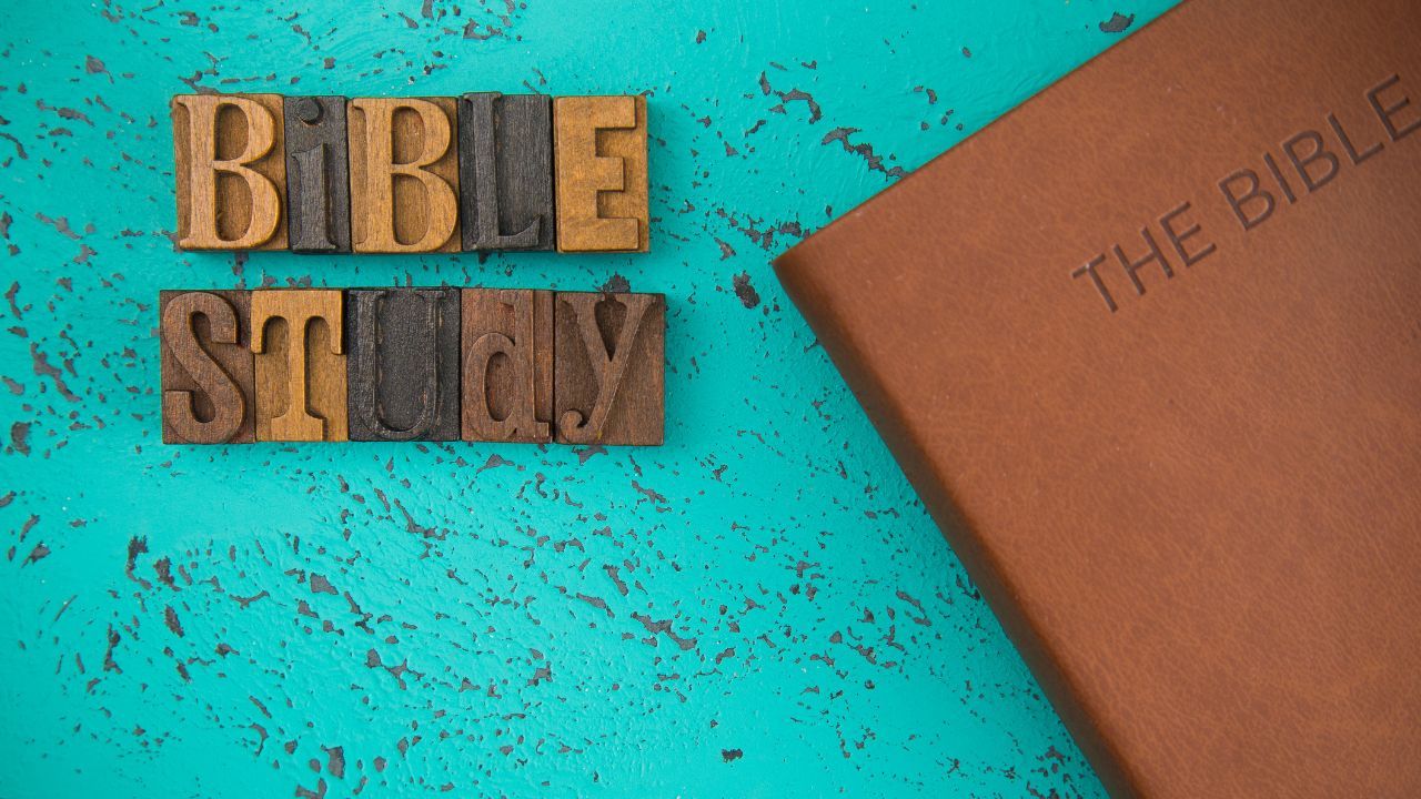 Wooden blocks spelling "Opening Prayer" next to a brown leather-bound bible on a textured turquoise background.