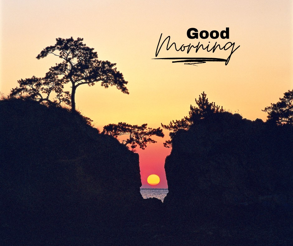 A serene sunrise viewed through a gap between rocky cliffs, with silhouetted trees and the text "Good Morning." The sky displays a gradient of warm colors from orange to pink. This image captures the tranquility of a natural landscape at dawn, ideal for good morning nature images, beautiful good morning nature images, and sunrise good morning nature images.