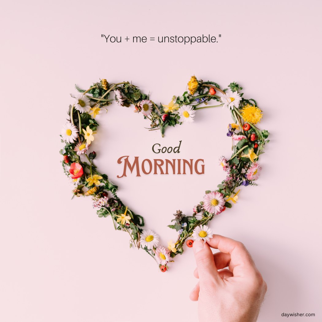 A beautiful good morning heart image featuring a heart shape made from a variety of colorful flowers and greenery. The background is light pink, and the text "Good Morning" is displayed in the center of the heart. Above the heart, the quote "You + me = unstoppable." is written. A hand is gently placing a flower on the heart, adding a touch of care and love. This image is perfect for sharing romantic and cheerful morning greetings.
